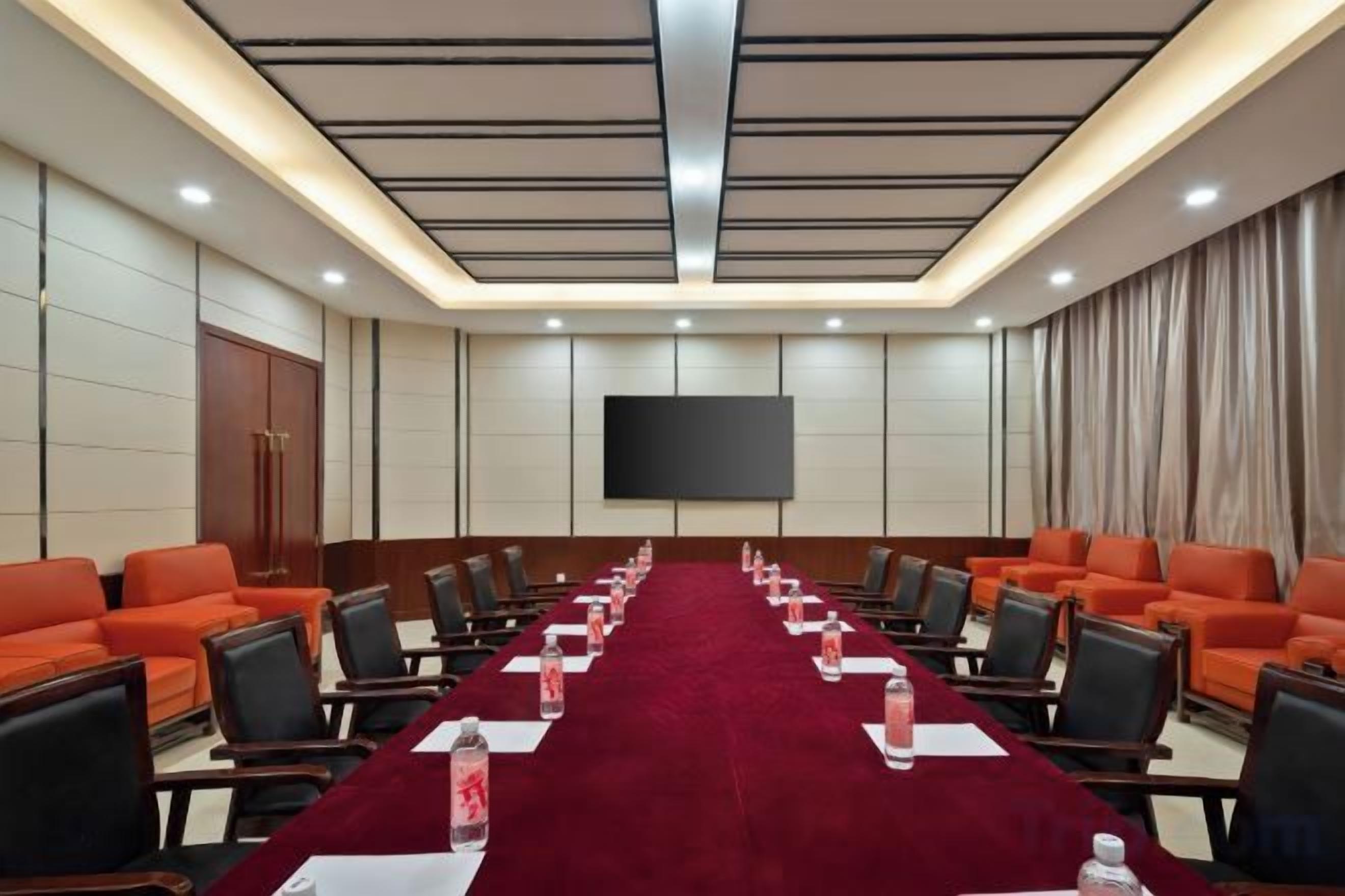 A conference room with a long table, chairs, and a large screen.