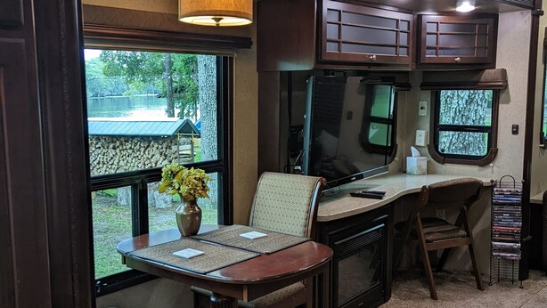 Een gezellig interieur van een camper met een eethoek, een keuken en een raam met uitzicht op een meer.
