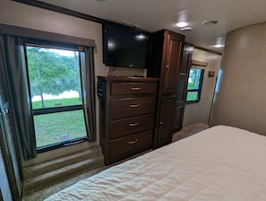 A bedroom with a bed, a dresser, a TV, and a window with an exit sign.