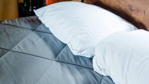 Ein Zelt mit einem Bett, ausgestattet mit einer grauen Bettdecke und weißen Kissen.
