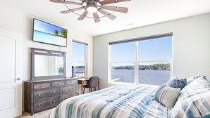 A bedroom with a large bed, a dresser, a desk, and a TV on the wall. - Island Life! Amazing Balcony-Views-Pool and Patio (Rocky Mount)