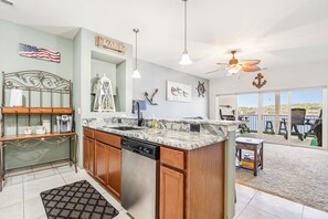 A kitchen with a dishwasher, wooden cabinets, and a marble countertop. There is a ceiling fan and a view of the outdoors through large windows. - Island Life! Amazing Balcony-Views-Pool and Patio (Rocky Mount)