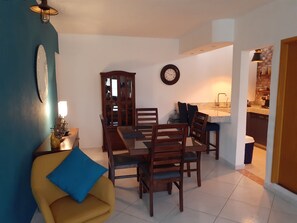 A dining area with a wooden table and chairs, a blue armchair, a cabinet, and a clock on the wall. - La Villa Palmier Your quiet House (Puerto Vallarta)