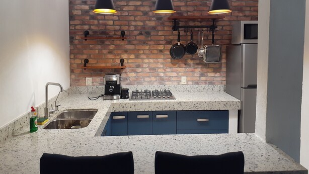 A kitchen with a brick wall, a gas stove, a sink, and hanging pots. - La Villa Palmier Your quiet House (Puerto Vallarta)