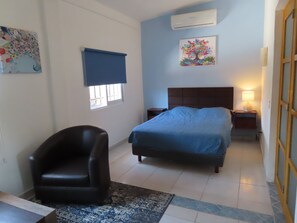 A bedroom with a bed, a chair, a nightstand, a lamp, and artwork on the walls. - La Villa Palmier Your quiet House (Puerto Vallarta)