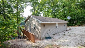 Une petite maison de plain-pied avec une terrasse en bois, une antenne parabolique et une allée gravillonnée.