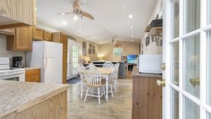 Une cuisine spacieuse avec des meubles en bois, un réfrigérateur blanc et un coin repas comprenant des chaises blanches et une table en bois.