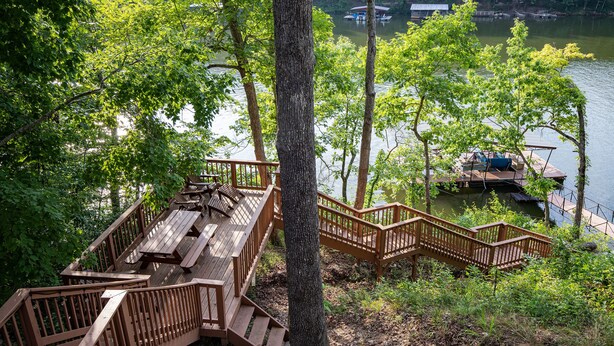Une terrasse en bois avec des tables de pique-nique et un escalier menant à un quai au bord d’un lac.