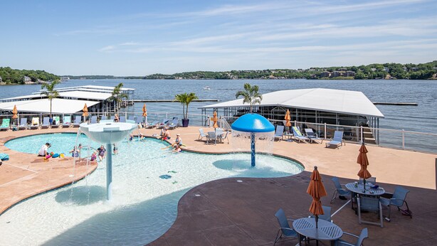 A pool area with lounge chairs and umbrellas, a water feature, and a view of the lake.