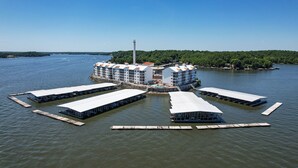 A waterfront hotel with multiple docked boats, a lighthouse, and a forested island in the background.