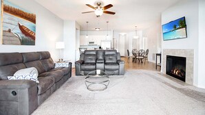 A living room with a leather sofa, a glass coffee table, a fireplace, and a ceiling fan.