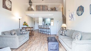 A spacious living room with a high ceiling, a dining area with bar stools, and a staircase leading to an upper level. - Amazing Views from Balcony, Loft & Gated Pool (Kaiser)