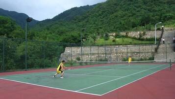 Una cancha de tenis con una red, rodeada de paisaje verde y montañas.