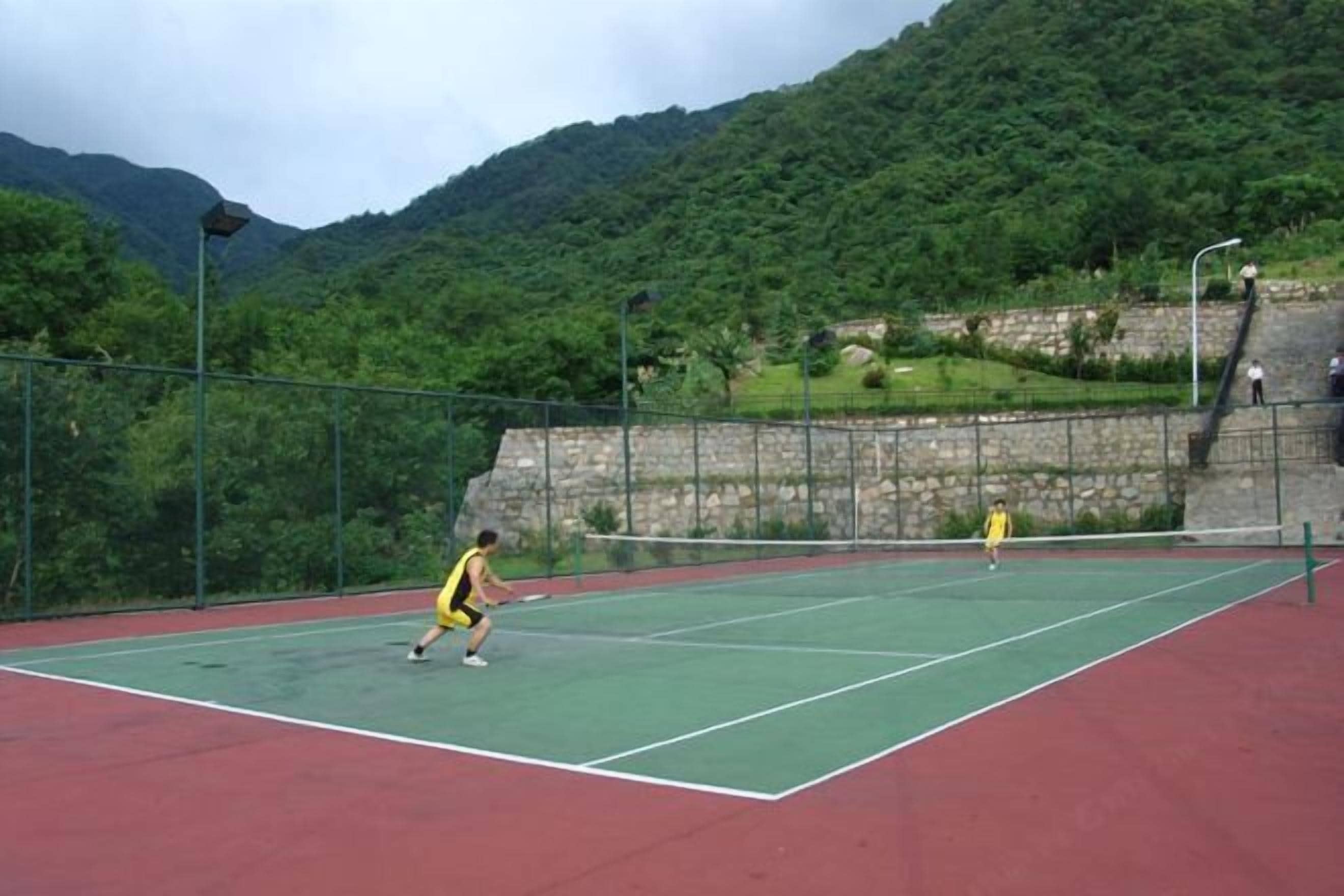 Una cancha de tenis con red, rodeada por un muro de piedra y vegetación.