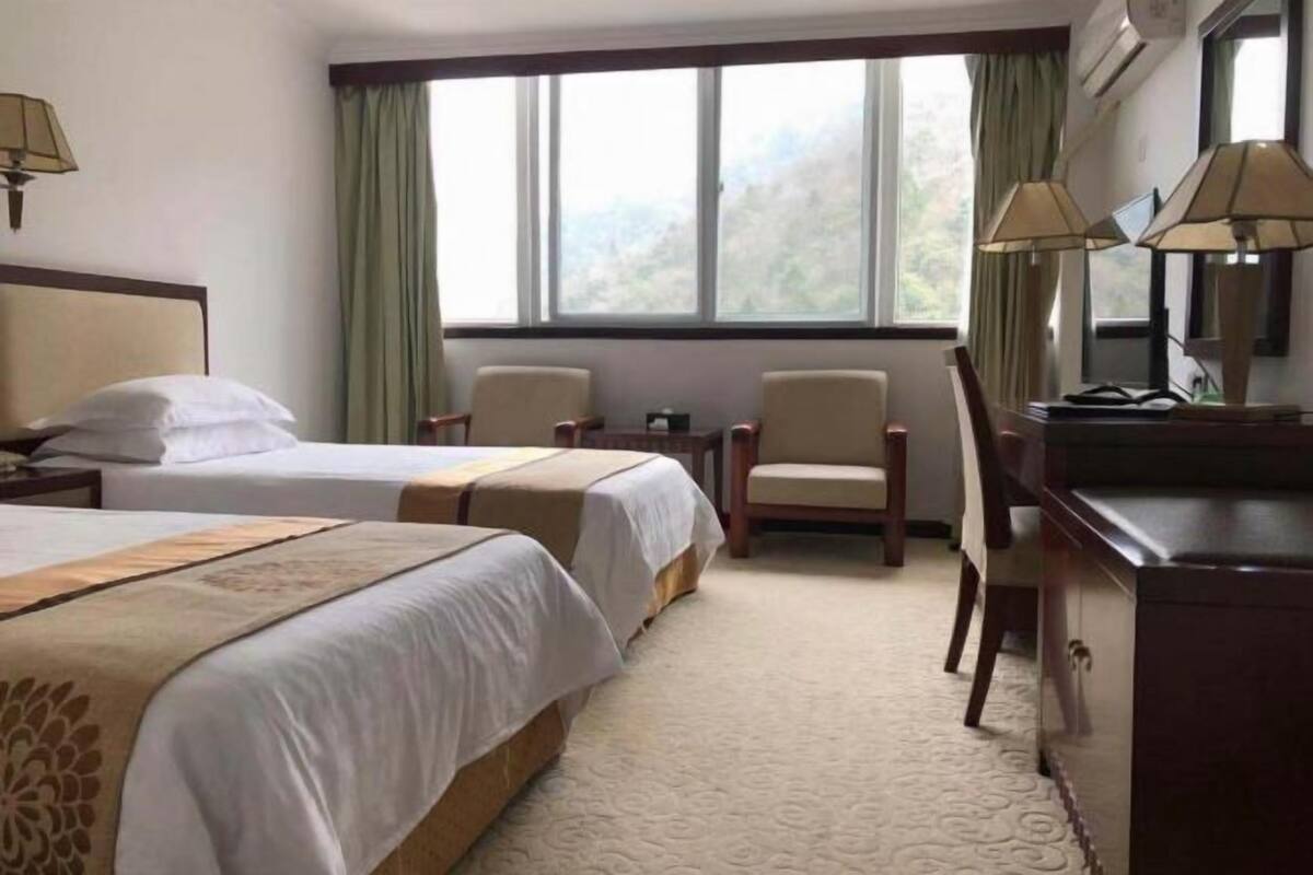 Une chambre d’hôtel avec deux lits, un bureau, deux chaises, une petite table et une fenêtre avec des rideaux.
