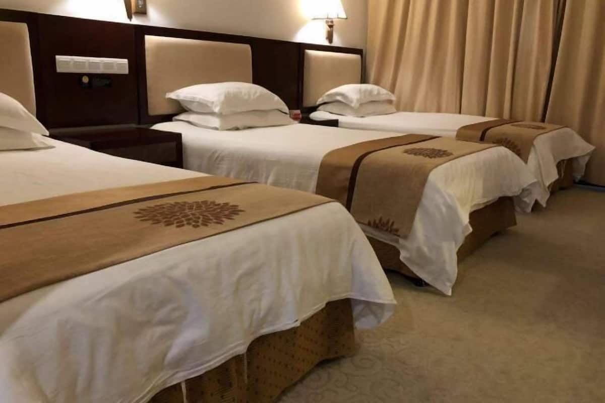 Une chambre d’hôtel avec trois lits, chacun doté d’une tête de lit, de draps blancs et d’un chemin de lit décoratif marron.
