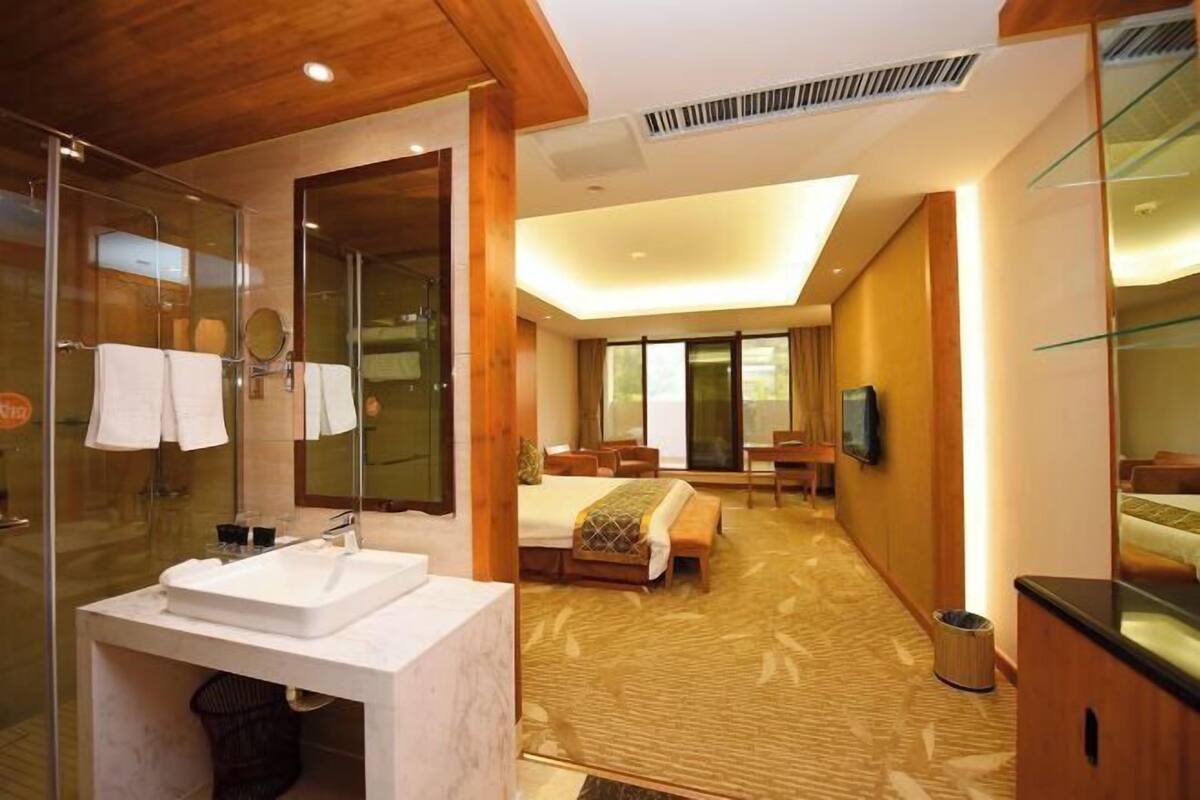 Une chambre d’hôtel moderne dotée d’une douche en verre, d’un grand lit, d’un coin salon et d’une télévision.