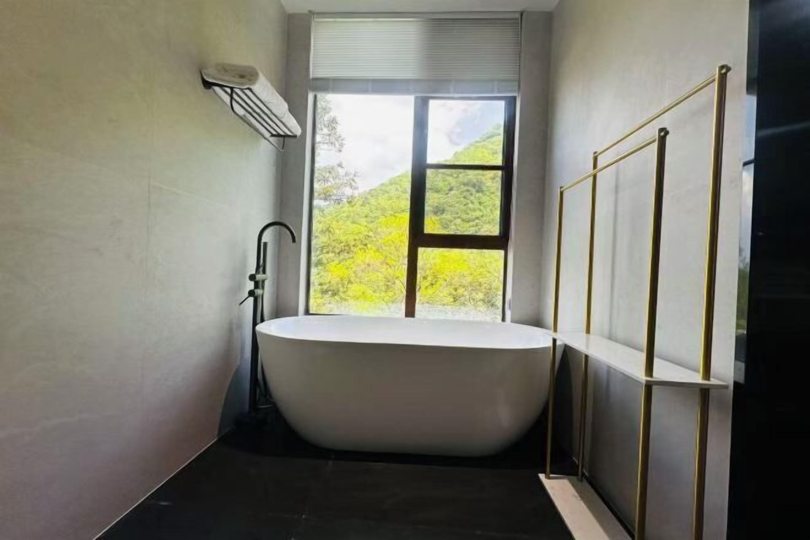 Un baño moderno con una bañera independiente, un ventanal con vistas a un paisaje verde y un perchero.