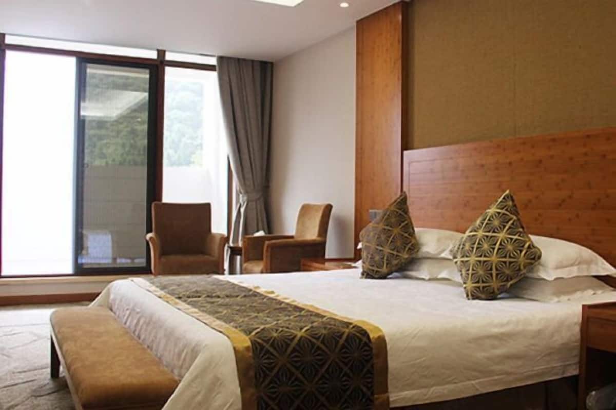 Une chambre d’hôtel avec un grand lit, un banc, une chaise et une vue sur l’extérieur grâce à une grande fenêtre.
