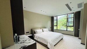 Quarto de hotel moderno com uma cama grande, uma mesinha de cabeceira de mármore, uma janela ampla com vista para o verde e um respiradouro no teto.