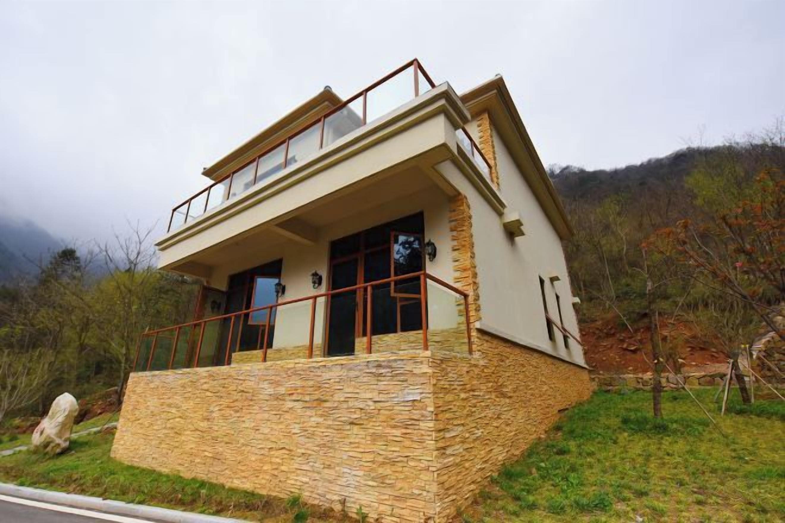 Un edificio moderno de dos pisos con base de piedra, ventanas grandes y un balcón.
