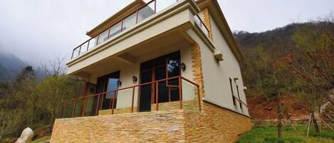 Un edificio moderno de dos pisos con base de piedra, ventanas grandes y un balcón.