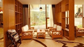 Um quarto com uma grande janela, estantes de madeira e um espaço de estar com mesas e cadeiras.