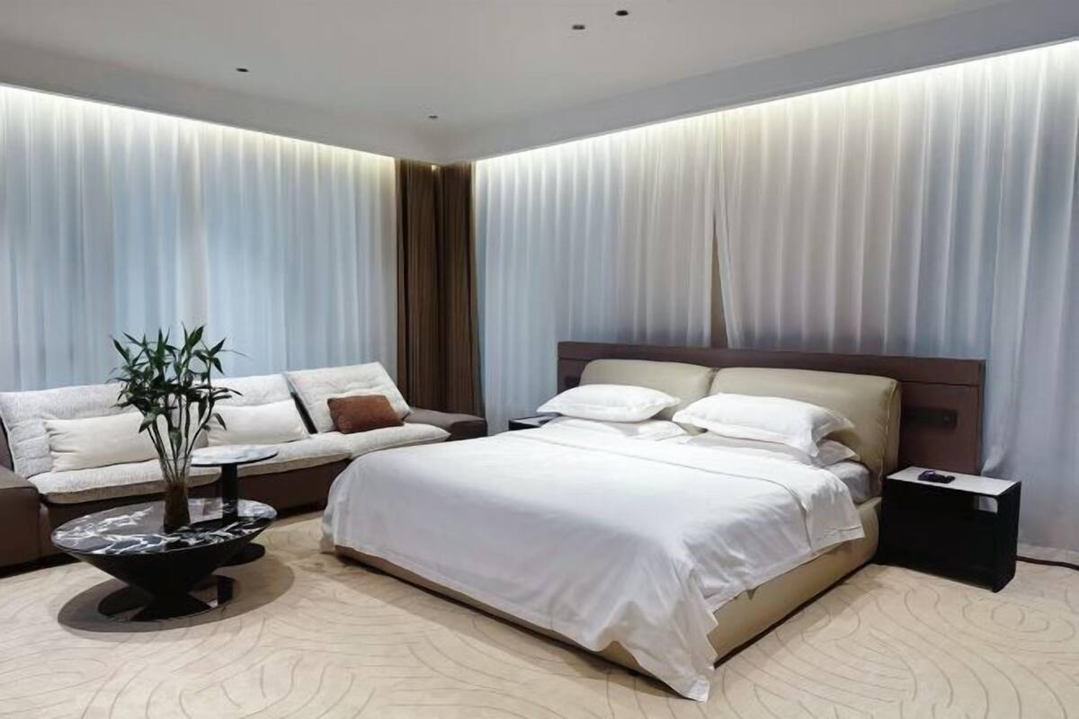Une chambre d’hôtel moderne comprenant un lit, un canapé, une table basse avec une plante et une table de chevet.