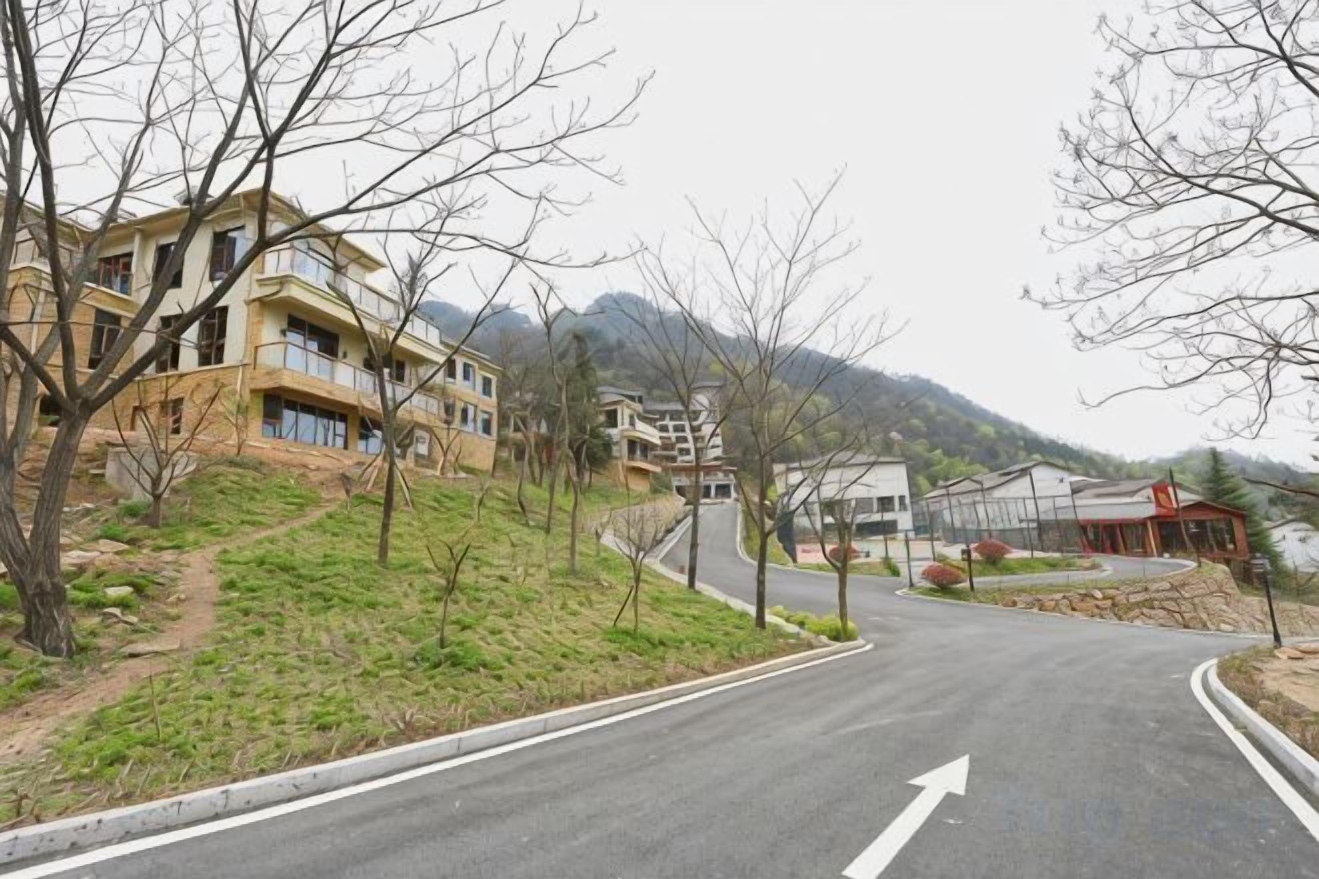 A road curving to the right with a building on the left and a mountain in the background.