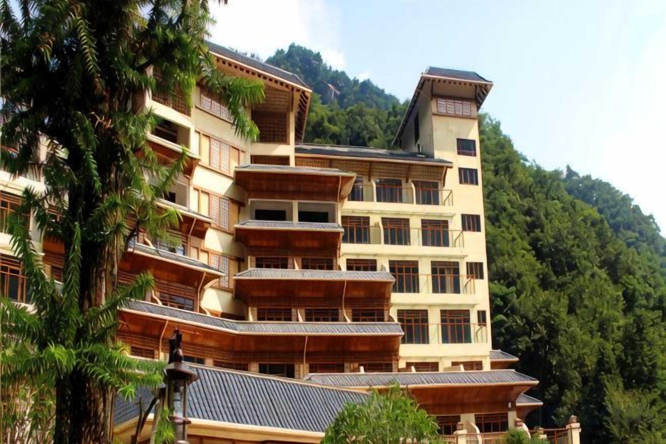 A multi-story building with balconies, surrounded by trees and hills.