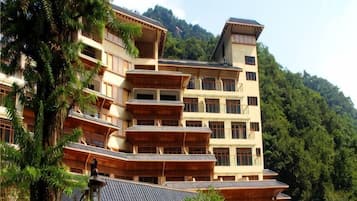 A multi-story building with balconies, surrounded by trees and hills.
