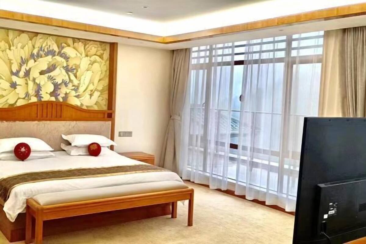 Une chambre d’hôtel avec un grand lit, une télévision, un élément décoratif mural et un balcon avec des rideaux.