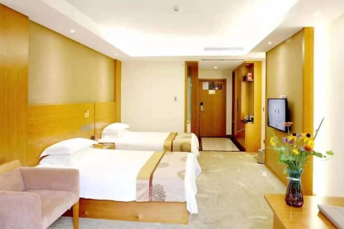 Une chambre d’hôtel avec deux lits, une télévision, un bureau et un vase avec des fleurs.