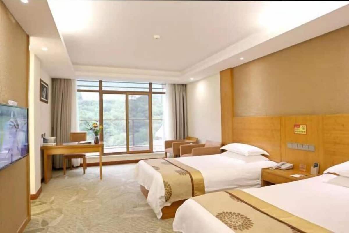 Une chambre d’hôtel avec deux lits, un bureau, une télévision et une grande fenêtre.