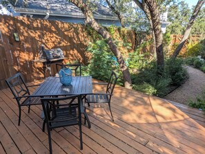A wooden deck with a table and chairs, surrounded by a wooden fence and trees.