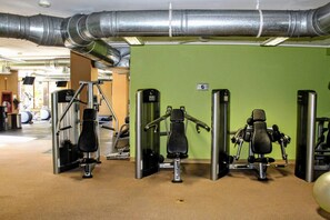 Een sportschool met fitnessapparatuur, een groene wand en zichtbare luchtkanalen.