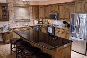 A kitchen with wooden cabinets, a stainless steel refrigerator, a microwave, and a large island with stools.