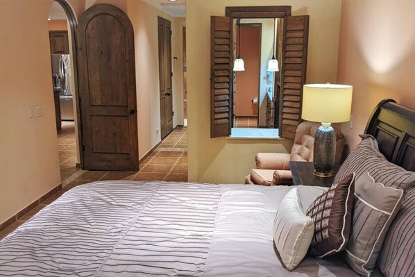 Habitación de hotel con una cama grande, una mesita de noche con lámpara, una silla y un espejo en la pared.