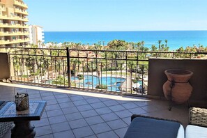 A balcony with a view of a swimming pool and the ocean.