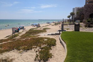 Uma praia com um caminho, guarda-sóis e um edifício ao fundo.