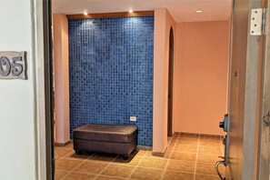 A hallway with a blue mosaic wall, a brown bench, and a door with a number sign.