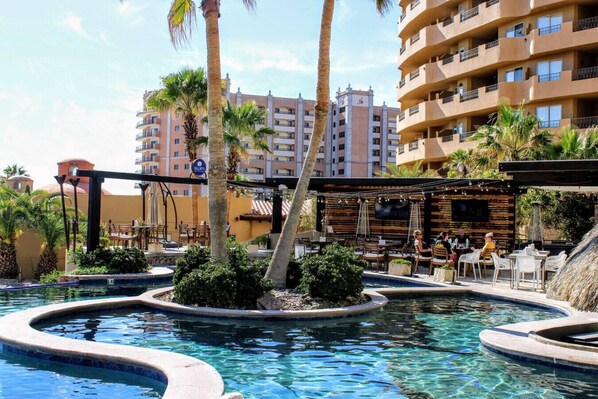 A resort pool area with palm trees, a bar, and a building in the background.