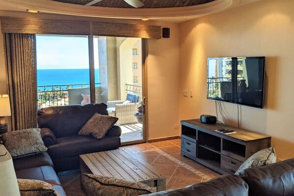 Una sala de estar con sofá, mesa de centro y televisor. Tiene un balcón con vista al mar.
