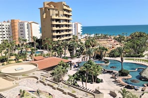 Een resort met een groot zwembad, palmbomen en uitzicht op de zee.