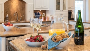 A kitchen counter with a bowl of strawberries, a pitcher of orange juice, a bottle of wine, and two glasses of white wine.