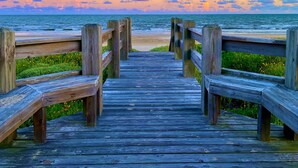 A wooden boardwalk leading to a beach with a sunset in the background.