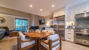 A modern kitchen with white cabinets, stainless steel appliances, and a dining area with a wooden table and white chairs. - Cozy mountain hideaway for hikers, skiers and chefs! (Truckee)