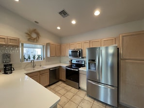 A modern kitchen with stainless steel appliances, wooden cabinets, and a white countertop. - Comfortable Desert Get-Away (Yuma)