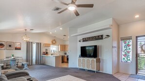 A spacious living room with a large TV, a ceiling fan, and a kitchen in the background. - Comfortable Desert Get-Away  (Yuma)
