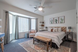 A bedroom with a bed, a chair, a desk, a ceiling fan, and a window with curtains.